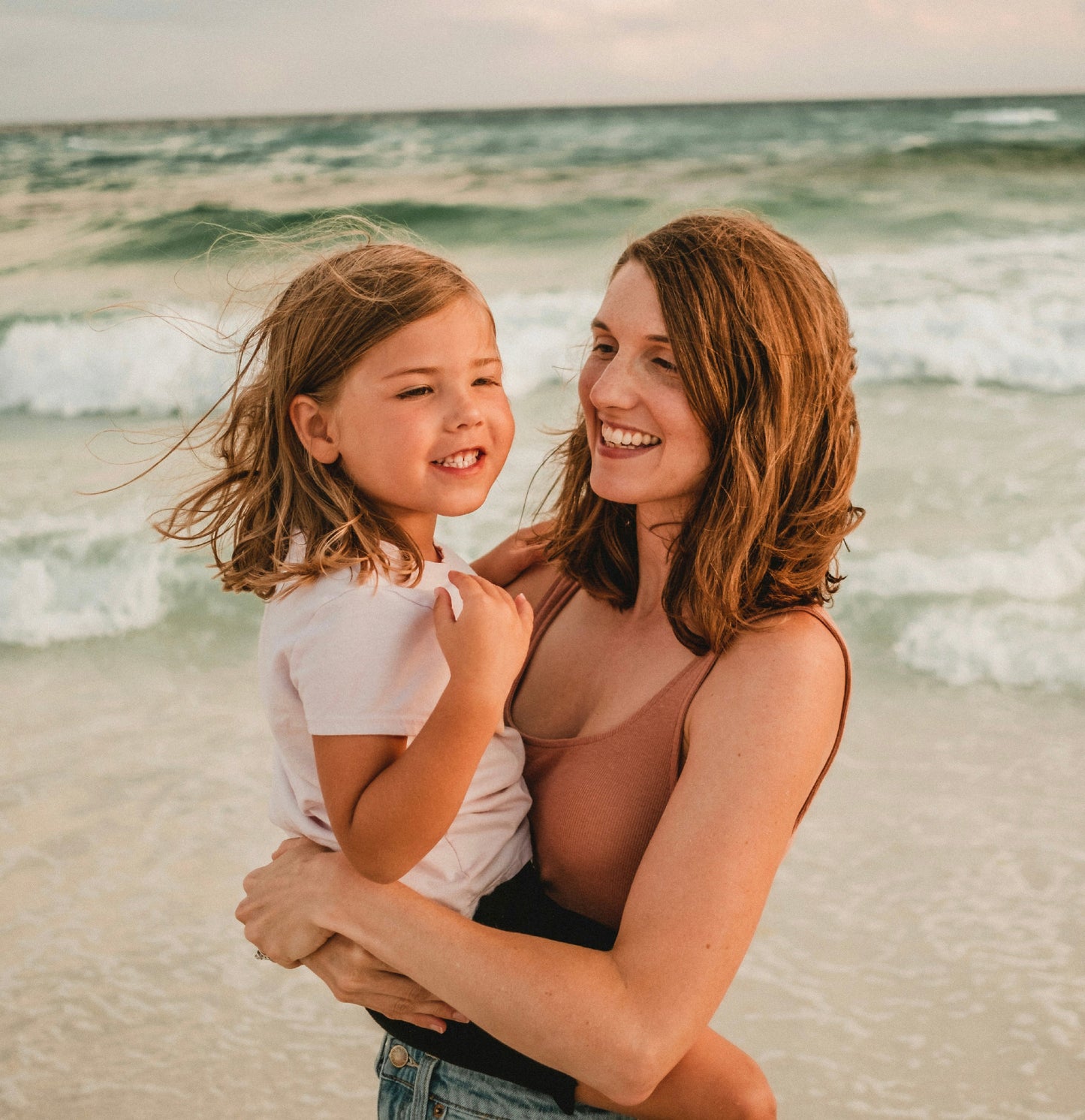 Woman holding a young girl on a beach with ocean waves in the background