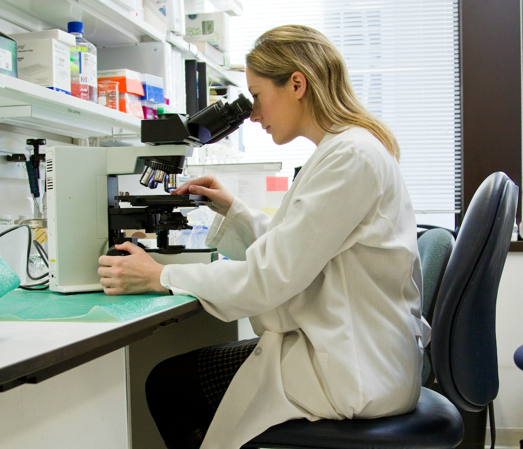 Person in a lab coat using a microscope in a laboratory setting
